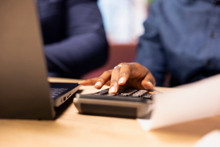 Man and woman reviewing bills and financial documents to track expenses, money management for a debt free lifestyle. Couple doing their household accounting with a calculator. Close up.の写真素材