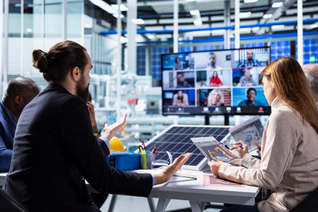 Photovoltaics factory managers look over schematics during online videocall, planning work on...