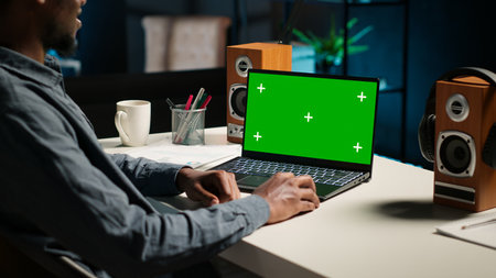 Teleworker at home editing documents next to mockup on his laptop, submitting reports and files before deadline. Black freelancer managing digital paperwork within the work platform. Camera B.の写真素材