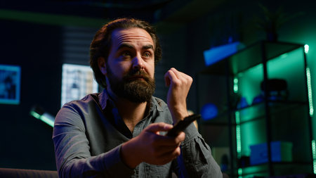 Frowning man watching sports match on TV, flabbergasted by surprising goal conceded by favorite team. Appalled supporter looking at football competition, reacting to player missing penalty, camera Aの写真素材