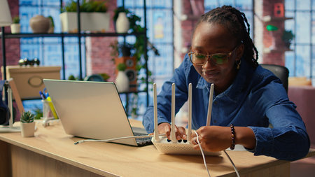 African american woman restarting her wireless router and checking network settings to resolve an...