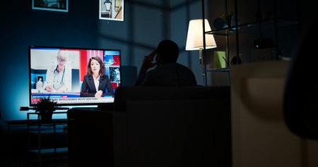 Curious spectator reading news coverage titles on smart tv set, sitting on couch and listening to...