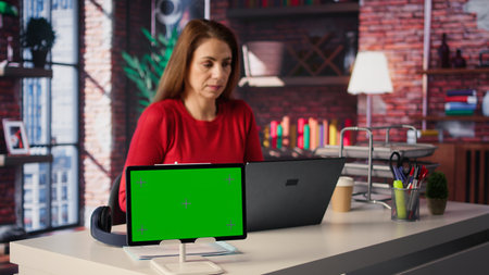 Mature woman reading forms and papers next to isolated screen and studying handwritten notes, surfing the web and staying connected for her freelance work tasks. Multitasking online. Camera B.の写真素材