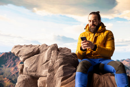 Nature lover relaxing on mountain top with his phone at a scenic viewpoint, looking out over the...