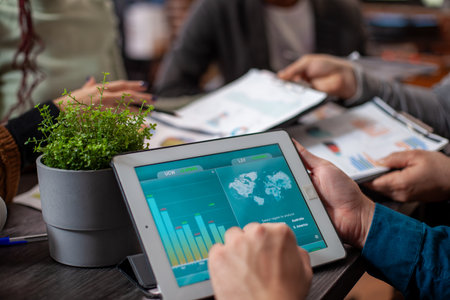 Caucasian person holds tablet displaying company marketing analysis with a green plant nearby on office desk. Closeup on device screen showing data graphs, being viewed by an individual at meeting.の写真素材