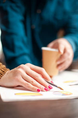 Closeup on hand of woman holding pen and pointing at financial documents near person with paper cup....