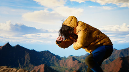 Traveler loses balance on a steep mountain peak as powerful winds knock him off course, falling and being unequipped in expedition. Hiker for the cold weather.の写真素材