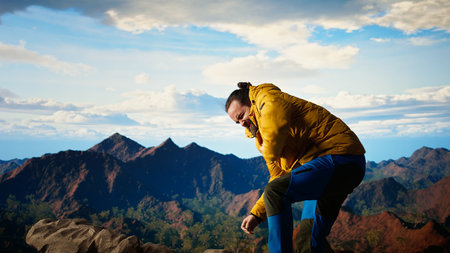 Hiker stumbles near the edge of a high altitude cliff, caught off guard by strong winds. Unequipped for the extreme conditions, losing balance on mountain top. Camera A.の写真素材