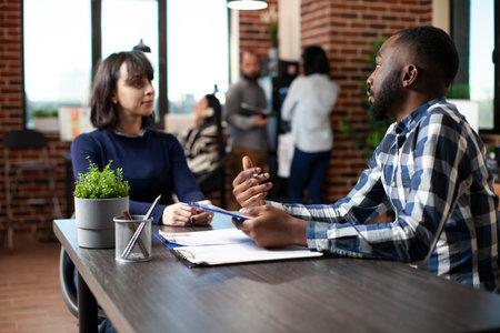 Young female job candidate listening attentively to african american office worker, discussing recruitment process at startup office. HR male representative with clipboard, interviewing a white woman.の写真素材