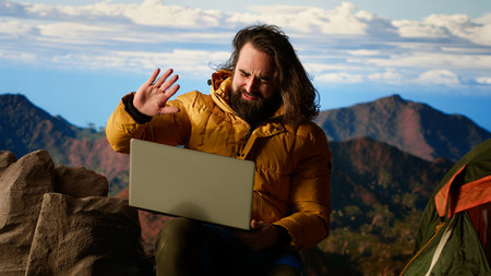 Mountain adventurer prioritizes his online business over safety, working on his laptop despite the extreme winds. The breathtaking landscape is overshadowed by his internet dependency.の写真素材
