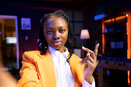 Influencer using filming equipment to do live broadcast for subscribers showing her new home studio design. Media star films herself for audience using phone camera in apartmentの写真素材