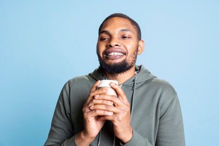Relaxed pleased young guy drinking a cup of black roast coffee, enjoying fresh tasty refreshment...