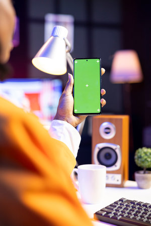 Freelancer taking break from work to watch videos on social media on green screen smartphone. Worker using social network website on mockup phone in home office, close upの写真素材
