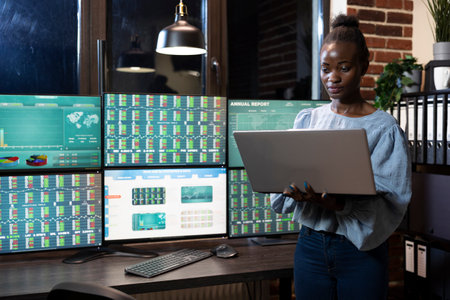 African American professional using her laptop, focuses on researching trading strategies. Young...