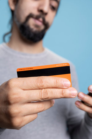 Pleased cheerful guy entering his credit card details on a website, feeling happy doing online...