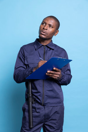 Security officer thinking of details to write for his duties on the job, taking notes to ensure safety at the mall. Bodyguard protecting the premises, uses clipboard papers for checklists.の写真素材
