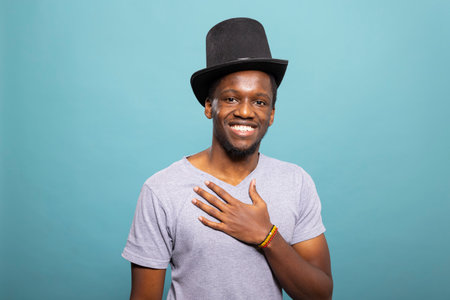 Young gentleman wearing a top hat and with his hand placed on his chest, standing against an...