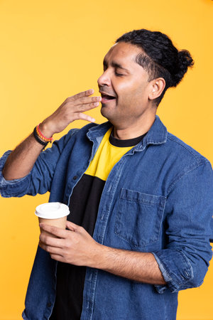 Sleepy man yawning and rubbing eyes sipping coffee to wake up and gain energy. Exhausted person feeling fatigued after sleepless night, drinking caffeinated beverage.の写真素材