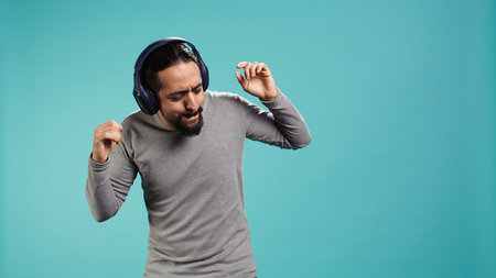 Happy person having fun, dancing on rhythm, listening music on headphones, enjoying leisure time. Cheerful man doing funky movements on songs, isolated over studio background, camera Bの写真素材
