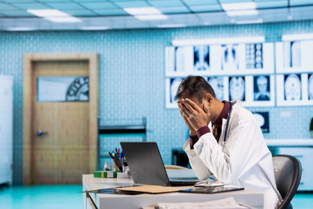 Stressed physician working late at night under pressure fighting to find a cure for a patient with dangerous disease, healthcare services. Overworked unhappy medic with anxiety at hospital.の写真素材