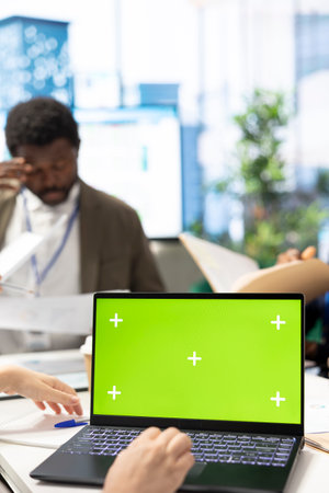 CEO uses laptop with green screen during a meeting with business associates, reviewing project development progress. Utilizing detailed analytics and mockup to ensure strategic objectives.の写真素材