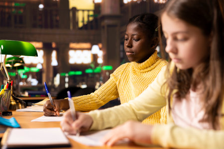 Diverse teens studying at a library table with textbooks and pens, immersed in school assignments for the literature class lesson. Productive study time at a desk using academic materials.の写真素材