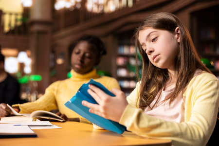 Preteen students focus on reading the required books at a study desk, developing their academic...