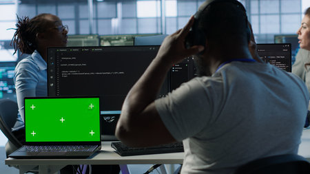 Isolated screen laptop next to programmer coding in server farm while listening music in headphones. Worker safeguarding hardware against unauthorized access with chroma key notebook, camera Aの写真素材