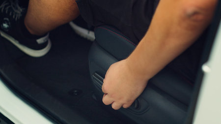 Close up of man in car pushing driver front seat forward using electric buttons. Person inside...