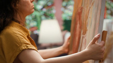 In a rustic atelier, painter mixes watercolor paint on a palette to create a masterpiece on canvas. Skilled woman painting with a brush and showing her creativity, artwork creation. Camera A.の写真素材