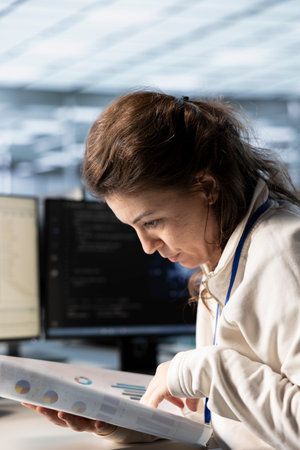 Management executive looking over paperwork in server farm to ensure compliance with industry standards and regulatory requirements. Close up of woman overseeing data center security protocolsの写真素材