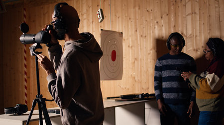 Firing range customer looking in zooming device to check if he shot bullseye next to instructor overseeing client. Person analyzing targets shot using magnifying lens during firearm practice, camera Aの写真素材