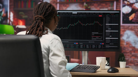 Day trader using PC to purchase and sell stocks, reading files, aiming to capitalize on market trends and fluctuations. Investor tracking stock forex trends on computer monitor, camera Bの写真素材