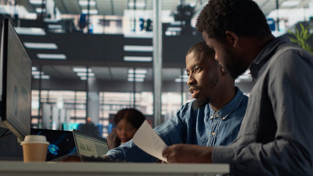 Business manager sits with a worker to review financial forecasts on pc, leading an analytics evaluation on project development. Achieving organizational goals for growth.の写真素材