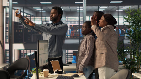 United african american employees taking photos at the corporate office, smiling and joking around on camera. Business team making memories with colleagues, friendly coworkers. Camera B.の写真素材