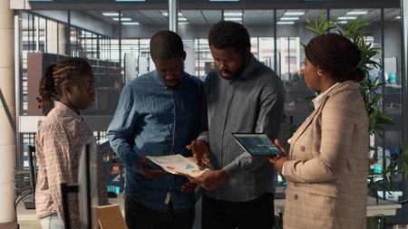 Black leader reviews company strategy with her team members in a modern corporate office, making key...