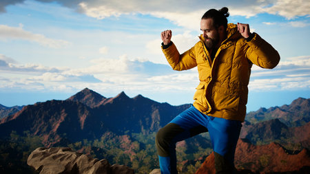 Happy climber cheering and feeling pleased while he stretches arms toward the sky, feeling the...