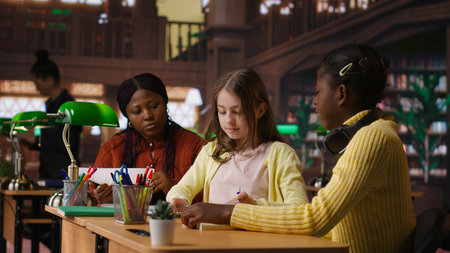 Preteens girls and their teacher collaborating on schoolwork at the library, focused on academic...