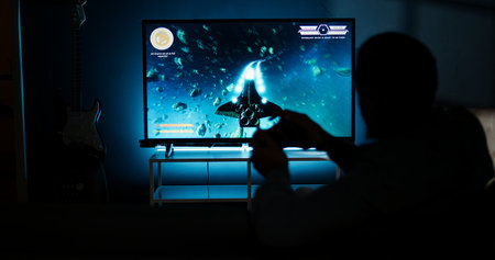 Young adult having fun with video games on his smart tv setup, connecting his console on lcd monitor television in living room and enjoying chill game night at home. African american gamer. Camera A.の写真素材