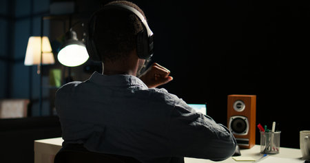 African american analyst works on accounting analysis while he is dancing, feeling the rhythm and checks financial balance. Remote worker listening to favorite groovy music on headphones. Camera A.の写真素材