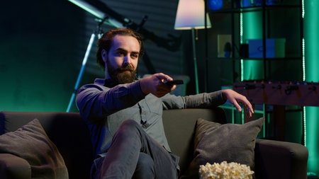 Man taking seat on sofa to watch television, getting entertained in relaxed home environment. Person...
