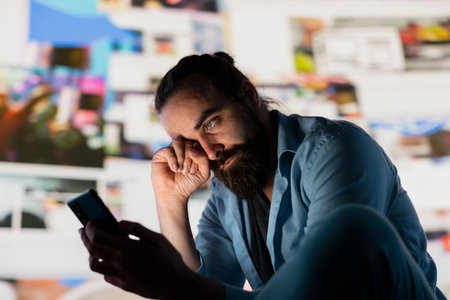 Distressed man suffers from social anxiety damage due to obsessive social media use. Young adult overwhelmed by excessive information and overload or cyberbullying affecting his self esteem.の写真素材