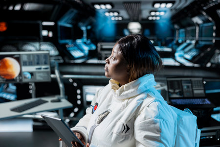 Woman in orbital station analyzing Mars planetary information on tablet. African american spaceship crew member doing Martian surface research using device to assist future planetary explorationの写真素材