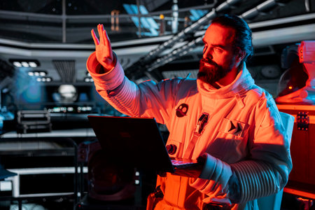 Spaceship crew member stressed by unknown hull breach causing alarm to sound. Worried cosmonaut reacts to system failure as radiation spike triggers emergency red lights inside orbital cockpitの写真素材