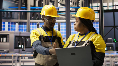 Solar panels factory team working together to fix gear, following maintenance procedures. Photovoltaics plant coworkers doing brainstorming, analyzes data on laptop to predict failures, camera Aの写真素材
