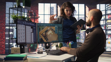 Architectural design team configures a floor plan on dual monitors, utilizing computer aided design tools. Colleagues use software for digital rendering and interior decoration remodeling. Camera A.の写真素材