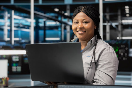 Portrait of smiling data center software developer using artificial intelligence neural networks. Cheerful server farm worker uses AI programming language on computer, configuring specialized hardwareの写真素材