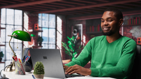 Black teleworker at home desk opening laptop to edit documents and solve daily tasks, updating...