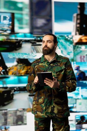 Young soldier working in command center with satellite surveillance integrating data, intelligence and AI warfare tactics for war planning in a national defense mission. Armed forces.の写真素材