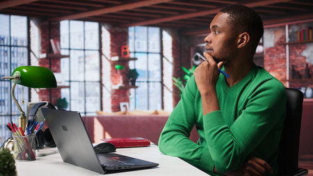 Black freelancer thinking about new solutions to increase profit and reach, multitasking to find ideas for financial growth. Young remote worker uses his creativity for success. Camera B.の写真素材